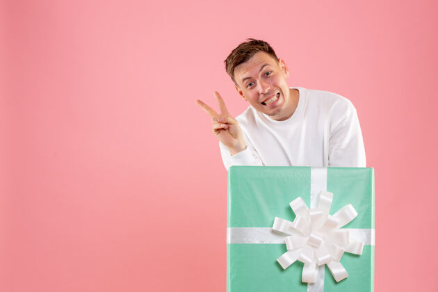 快乐一个年轻人躲在礼物里 在粉红色的墙上摆姿势商务十二月礼物