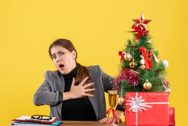 桌子正面图大眼睛女孩坐在桌子旁 抱着胸前的圣诞树和鸡尾酒礼物圣诞节鸡尾酒举行