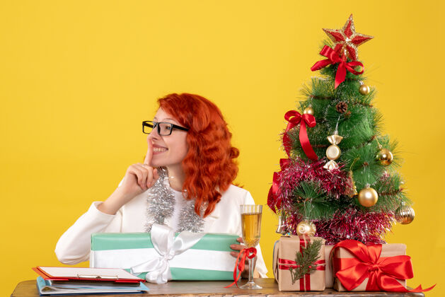 前面前视图：女医生拿着圣诞礼物和黄色背景上的圣诞树坐着情绪女医生圣诞节