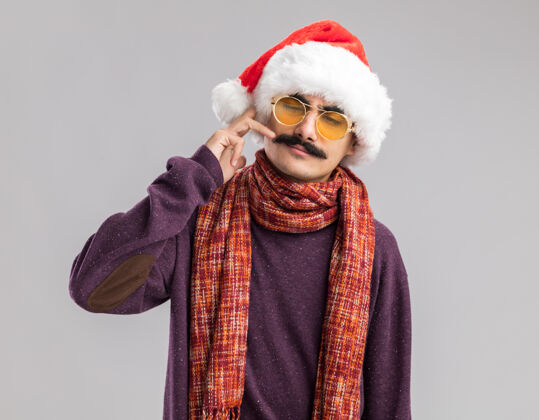 温暖一个留着胡子的男人戴着圣诞老人帽 戴着黄色眼镜 脖子上围着一条暖和的围巾 手站在白色的背景上 看起来很自信手势圣诞圣诞老人