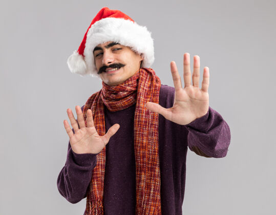 圣诞快乐一个留着胡子的男人戴着圣诞老人帽 脖子上围着一条暖和的围巾 看上去很困惑 用手做着防御的手势困惑制造周围