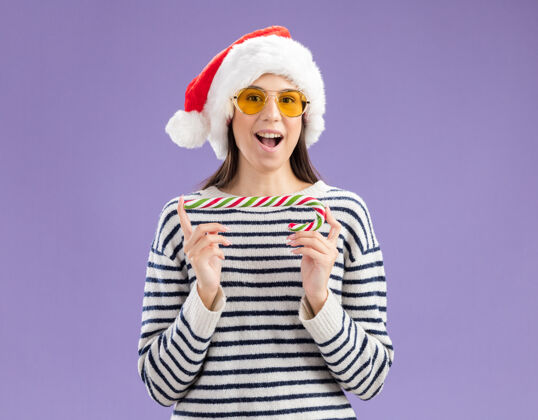 太阳戴着太阳眼镜 戴着圣诞帽 拿着糖果手杖的兴奋的白人女孩年新年年轻