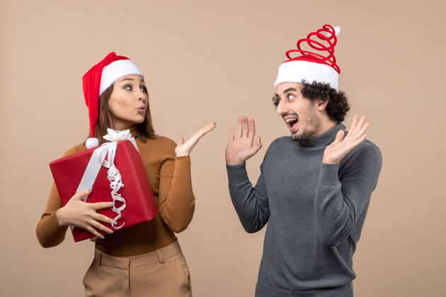 亲吻新年气氛喜庆的概念与有趣可爱的情侣戴着红色圣诞老人帽送上灰色的亲吻女孩帽子节日圣诞老人