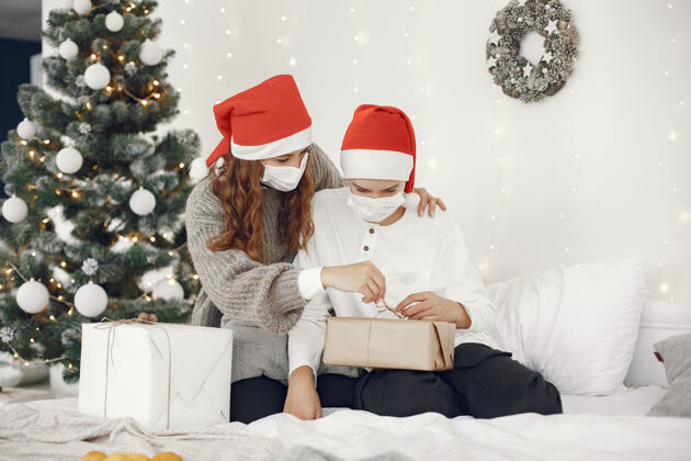 十二月为圣诞节做准备的人冠状病毒主题妈妈和儿子玩穿白毛衣的男孩装饰圣诞树小