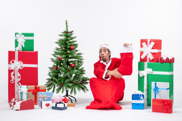 礼物圣诞老人坐在地上 拿着圣诞袜 靠近礼物和装饰过的圣诞树圣诞老人快乐快乐