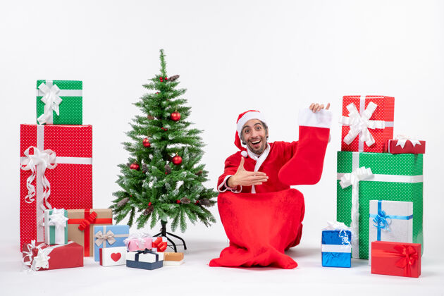 圣诞树圣诞老人坐在地上 指着圣诞袜旁边的礼物和装饰圣诞树圣诞老人礼物圣诞老人