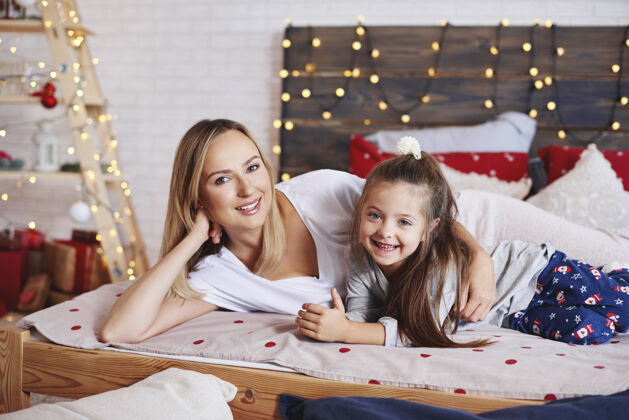 睡衣母女俩在床上度过圣诞节早晨的画像圣诞树父母微笑