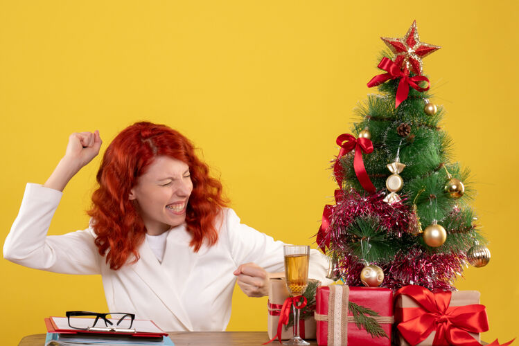 黄色女工人坐在桌子后面 拿着圣诞树和黄色的礼物女办公室坐着