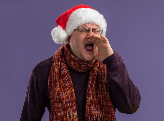 保持戴着眼镜 戴着圣诞帽 脖子上围着围巾的成年男子 手放在嘴边 看着旁边的人 大声对紫色背景上孤立的人喊叫附近围巾眼镜