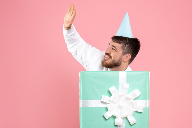 圣诞节年轻人站在礼物盒内 在粉色墙上打招呼的正面图丝带盒子前面