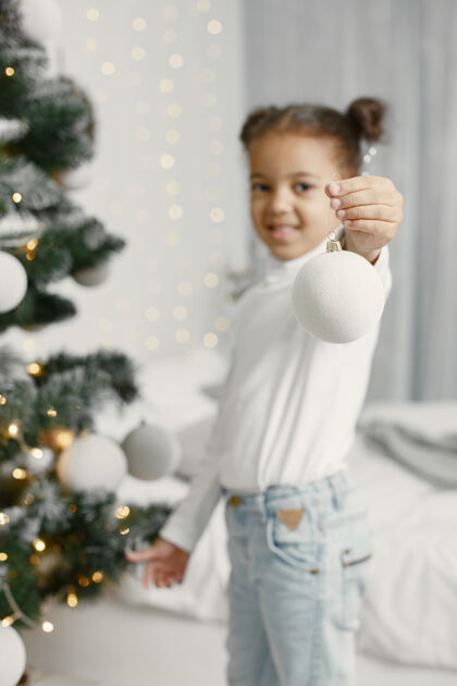 女儿穿白色毛衣的孩子站在圣诞树旁的女儿盒子室内肖像