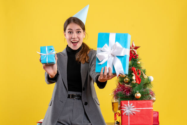 礼物前视图喜出望外的女孩与党帽举行圣诞树附近的圣诞礼物和礼物鸡尾酒圣诞节树举行