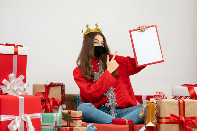 年轻女孩穿着红色毛衣的年轻女孩展示文件坐在礼物旁边 白色的面具上戴着黑色的面具礼物欢乐文件