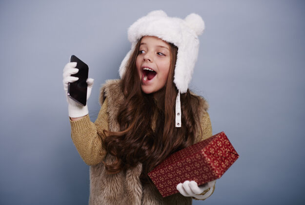 乐趣带着手机和礼盒的兴奋女孩圣诞礼物看肖像