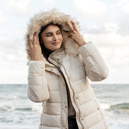 独自海滩上穿着冬装的笑脸女人的正面图冬天夹克冒险