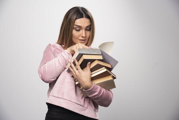 携带穿着粉色运动衫的女孩手里拿着一堆书 正试着用放大镜看最上面的那本人教育女