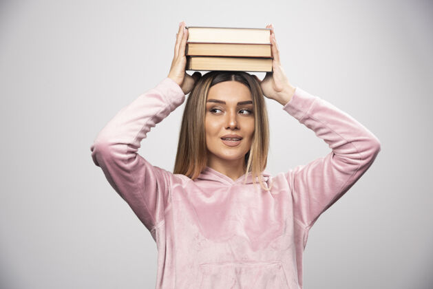 聪明一个穿着粉色衬衫的女孩把书举过头顶女性员工摆姿势