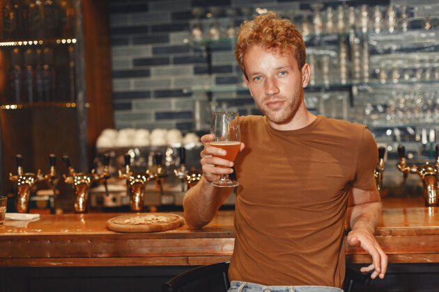 液体有魅力的年轻人站在吧台后面一个穿着棕色t恤的男人手里拿着一个玻璃杯西装威士忌头发