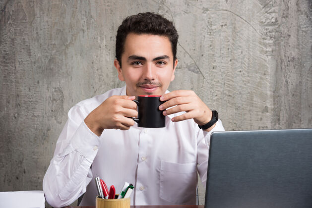 笔记本电脑商人在办公桌旁端着一杯茶书喝酒办公室