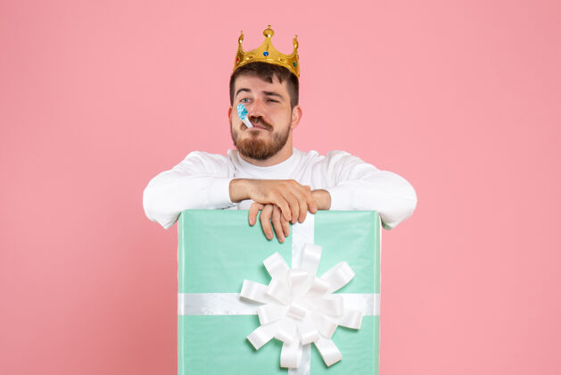 微笑年轻人在礼物盒内的正面视图 粉红色墙上有皇冠情感前面人