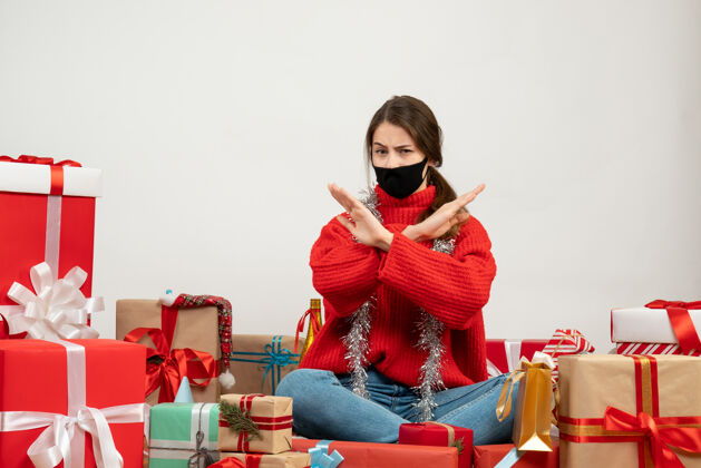 欢乐戴着红色毛衣和黑色面具的年轻女孩双手交叉坐在白色的礼物上周围人红