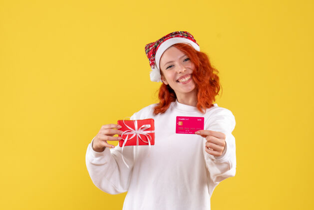 年轻女性圣诞礼物和黄墙上银行卡的年轻女子的正面图人圣诞节礼物