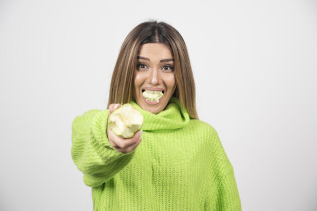 成人穿着绿色t恤的年轻女子正在吃苹果举行人健康