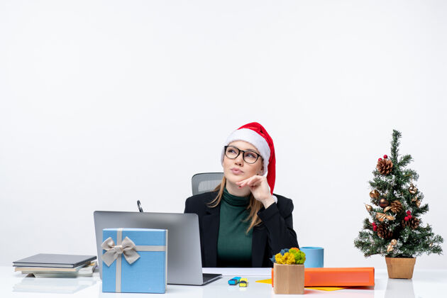 礼物一个金发碧眼的女人 戴着圣诞老人的帽子 坐在桌子旁 手里拿着圣诞树和礼物金发女人女商人企业家