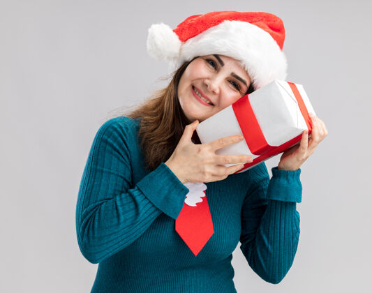 成人高兴的成年白人妇女与圣诞帽和圣诞领带举行 并把在白色背景与复制空间隔离头上的圣诞礼品盒圣诞快乐圣诞老人圣诞节