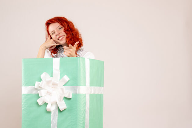 可爱一个年轻女子躲在一个白色的墙内礼物的正面视图庆祝人圣诞快乐