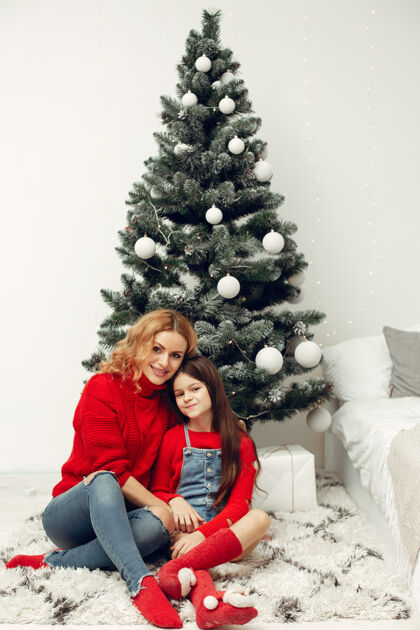 节日人们在为圣诞节做准备母亲在和女儿玩耍一家人在节日的房间里休息孩子穿着红色毛衣牛仔裤花环室内