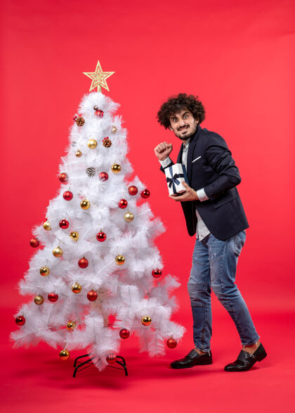 圣诞树新年庆祝与年轻人展示他的礼物附近愉快地装饰白色圣诞树上的红色镜头年轻人镜头男人