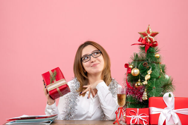 粉色女工人坐在粉红色的圣诞礼物和圣诞树旁的正视图肖像礼物工作