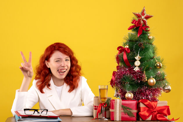 树女工人坐在桌子后面 手里拿着圣诞礼物和黄色的圣诞树办公室工人坐着