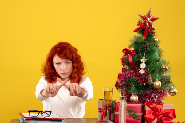 礼物女工人坐在桌子后面 手里拿着圣诞礼物和黄色的圣诞树桌子不高兴安排