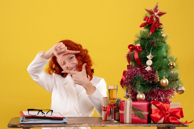 办公室女工人坐在桌子后面 拿着圣诞树和黄色的礼物女女工人圣诞节
