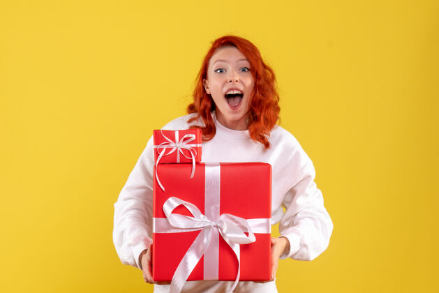 女人黄色墙壁上年轻女子拿着圣诞礼物的正面图漂亮成人微笑