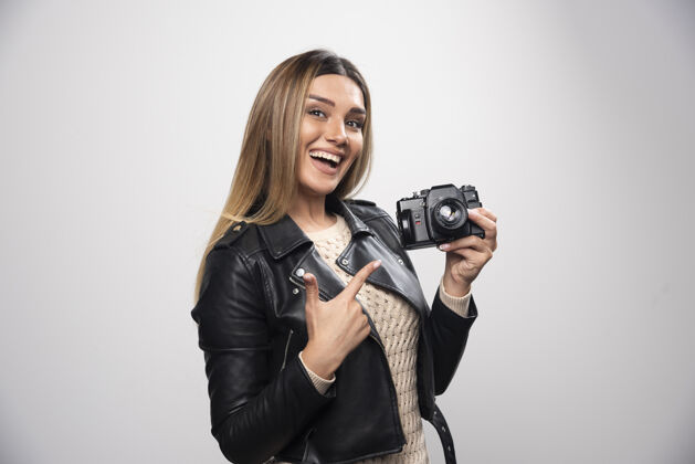 休闲一位身穿黑色皮夹克的年轻女士 以积极微笑的态度用相机拍照数码年轻人摄影师