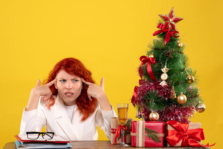 工人女工人坐在桌子后面 手里拿着圣诞礼物和黄色的圣诞树坐着办公室圣诞节