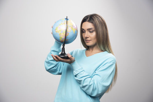 职员穿着蓝色运动衫的金发女孩手里拿着地球仪 仔细地查看着地球地图年轻人休闲地理