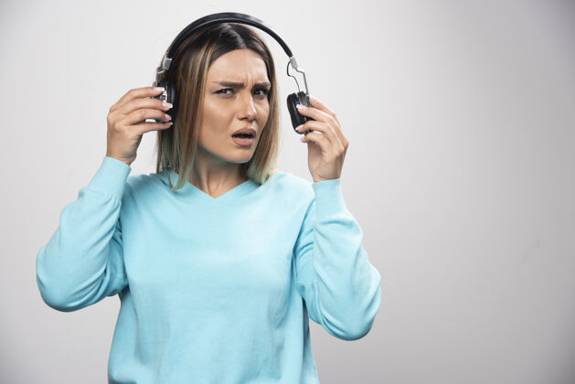 音乐穿着蓝色运动衫的金发女孩听着耳机 却不喜欢音乐女不同意人