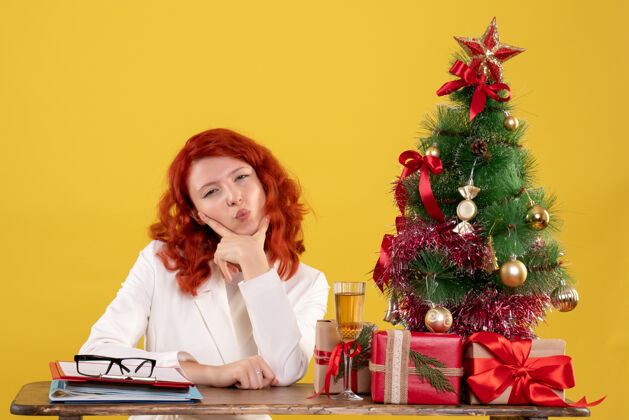 小女工人坐在桌子后面 手里拿着圣诞树和黄色的礼物女工人坐着插花