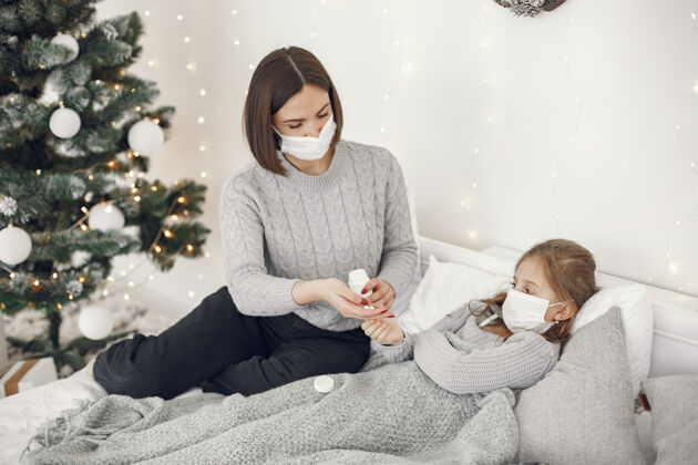 生病儿童中有冠状病毒母亲带着女儿孩子躺在床上戴着医用口罩的妇女小床发烧