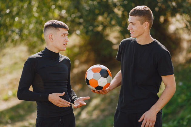 足球男子在公园玩足球迷你足球锦标赛穿黑色运动套装的家伙草地校园活动