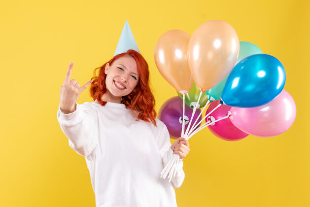 女人手持彩色气球的年轻女子在黄色墙壁上摆姿势的前视图年轻庆祝女性