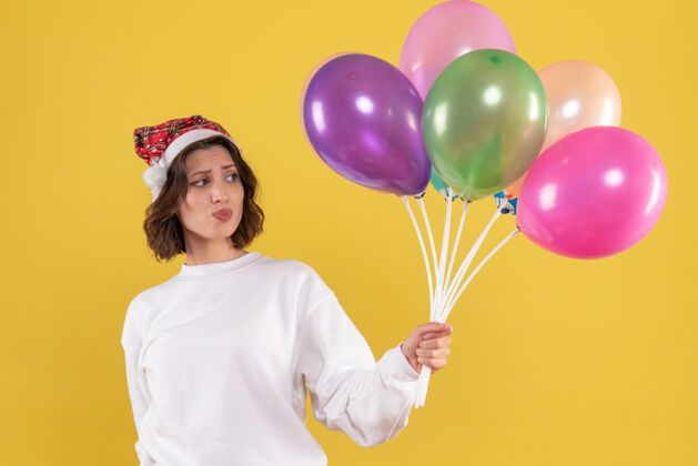 情感黄色墙壁上手持彩色气球的年轻女子的正视图女性生日女人