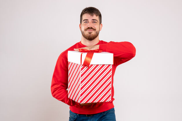 年轻前视图中的年轻人在红衫举行圣诞礼物在一个白色的墙壁框年轻男性圣诞节微笑