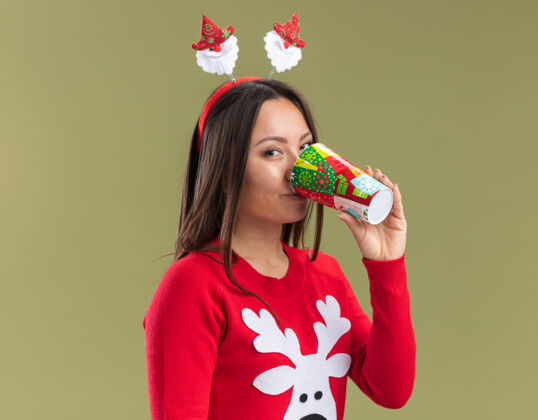 高兴高兴的年轻亚洲女孩穿着圣诞头发箍饮料孤立的橄榄绿背景圣诞节年轻篮球