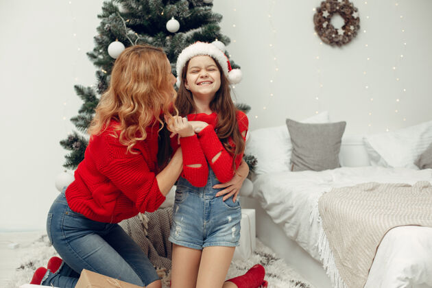 节日人们在为圣诞节做准备母亲在和女儿玩耍一家人在节日的房间里休息孩子穿着红色毛衣杉木盒子装饰