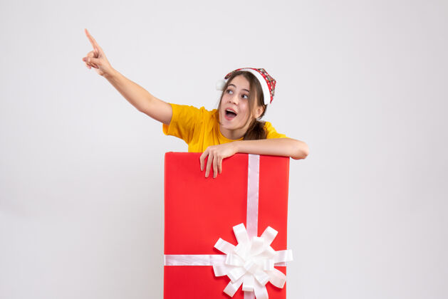礼物戴着圣诞帽的大眼睛女孩指着站在白色圣诞礼物后面的东西漂亮什么的指着